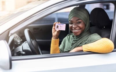 Cheerful woman sitting in her car and showing new driver licence.