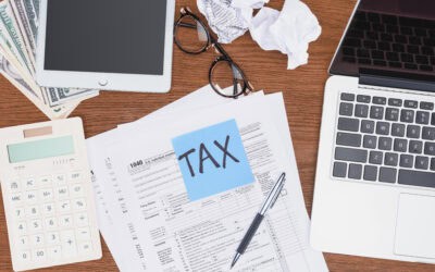 top view of tax forms, digital devices and blue card with 'tax' word on desk