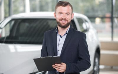 Smiling manager holding folder in car showroom.